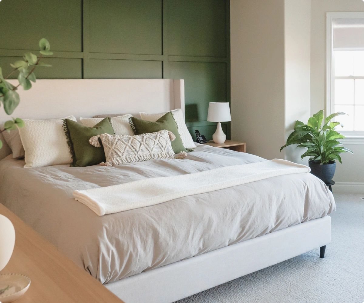 Rich green and white themed bedroom. Made bed with decorative pillows.